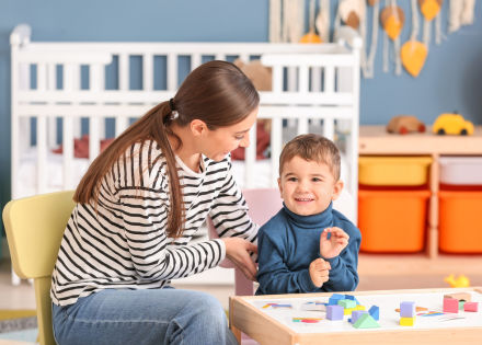 Mother and son smiling. They are sitting at a small table with wooden brick toys on it. 